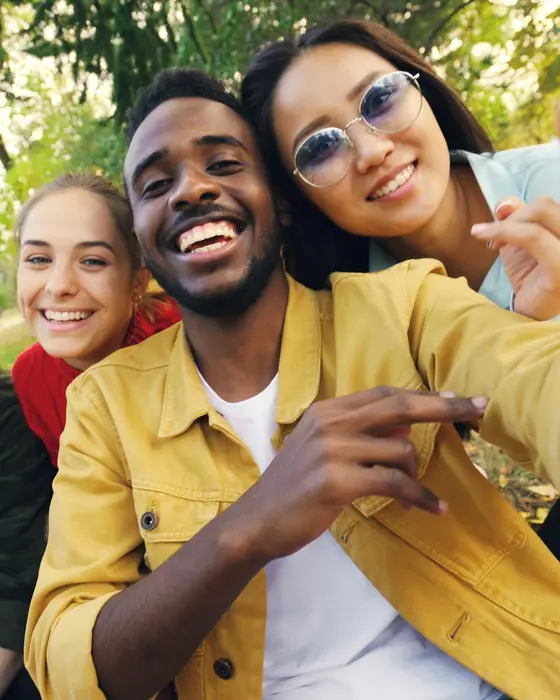 Un groupe de jeunes amis souriants prend un égoportrait dans un parc.