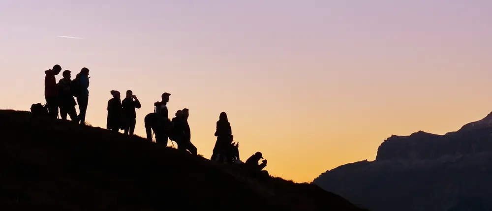 Silhouettes d’un groupe de jeunes au sommet d’une colline, au lever du soleil.
